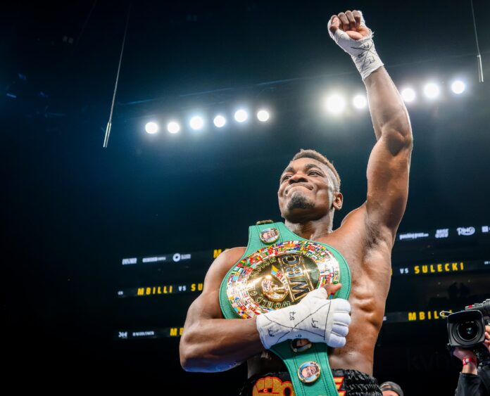 Christian Mbilli raises his hand while wearing the WBC championship belt after winning a boxing match