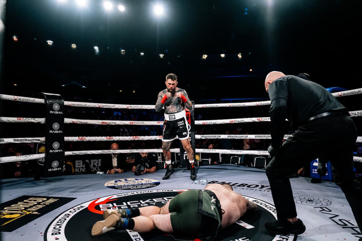 Branko Busick stands in the ring during his bout against Anthony Mendoza while Mendoza lies on the floor as the referee attends to him