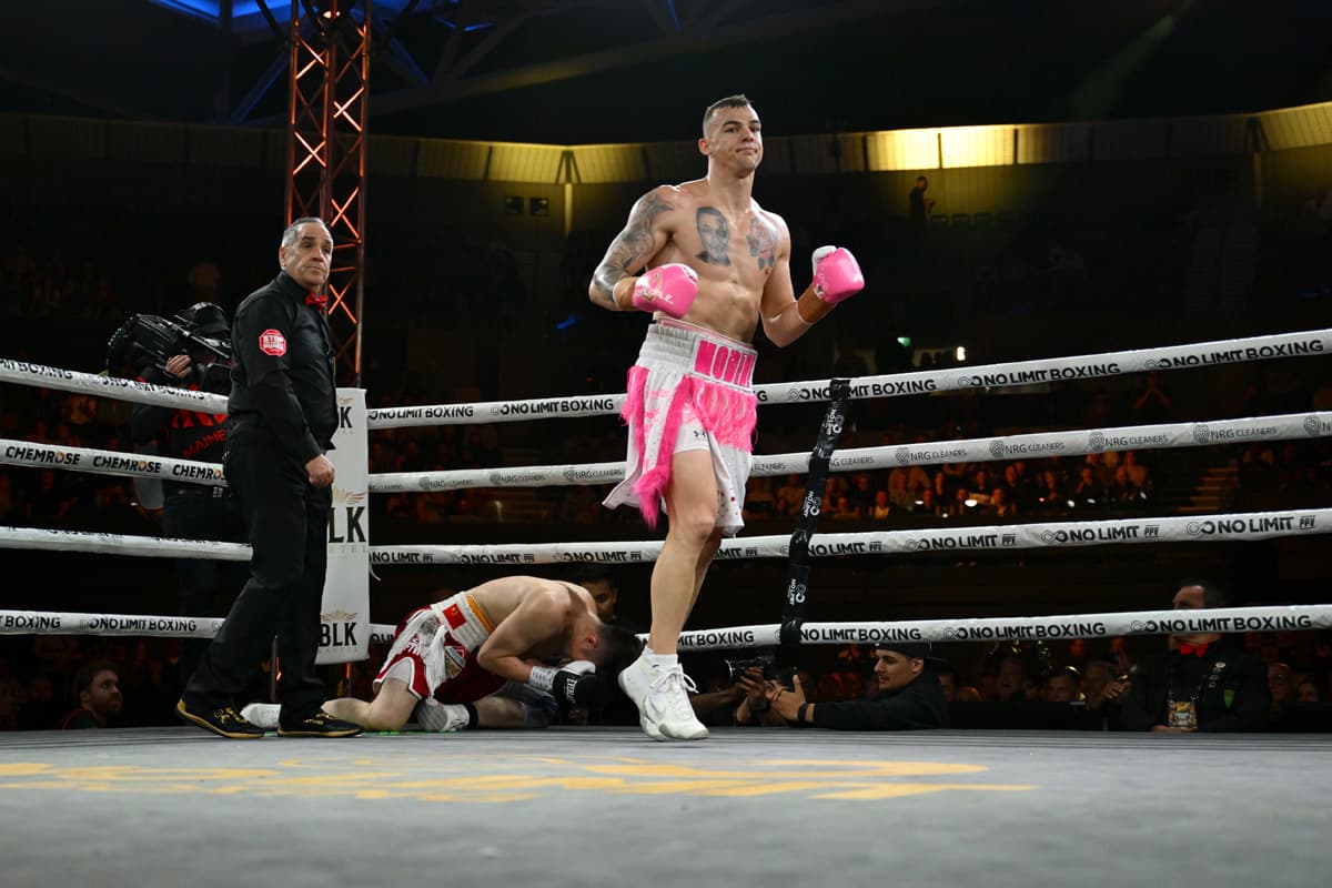 Luke Modini walks away as Peng Qu lies on the canvas with the referee nearby