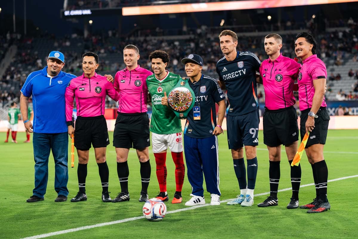 Isaac Cruz stands on the field with officials and members of both teams before the game