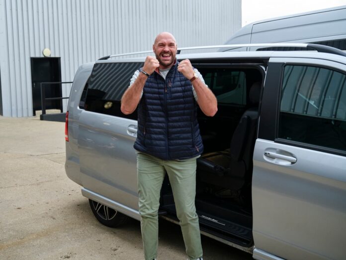 Tyson Fury poses in a boxing stance with his hands raised in front of a minibus in London
